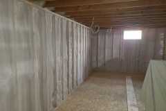 Unfinished basement framing with spray foam insulation applied between wall studs and open ceiling joists by Classic Spray Foam.
